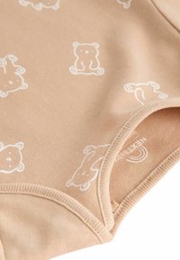 Beige bodies i mjuk bomull med ett vitt björnmönster. Halsringningen och benöppningarna är kantade med en fin ribbad kant.