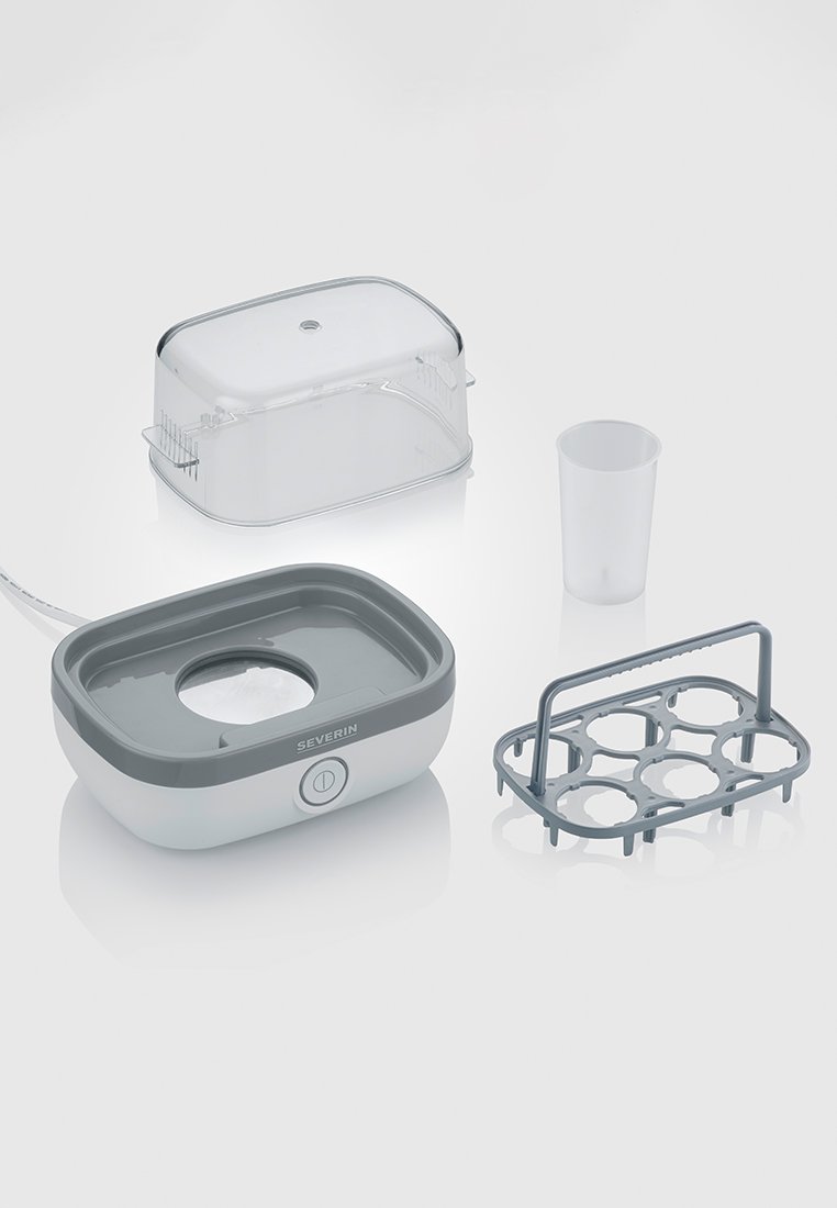 Appareil électrique en blanc et gris avec une base rectangulaire, un couvercle transparent, un verre doseur et un support à œufs gris comportant six sections.