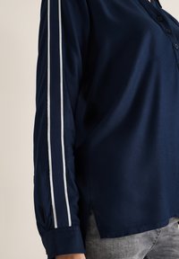 Camicia blu navy con bottoni in tessuto liscio, caratterizzata da strisce laterali bianche, maniche lunghe e dettaglio con spacco all'orlo.