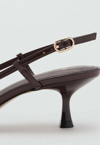 Hnedé latherové slingback topánky na opätku s zlatou oválnou prackou a krátkym zužujúcim sa opätkom na neutrálnom pozadí.