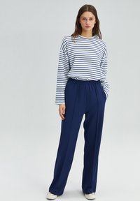 Striped long-sleeve shirt in white and navy, paired with navy elastic waistband trousers. Simple, relaxed fit with side pockets.