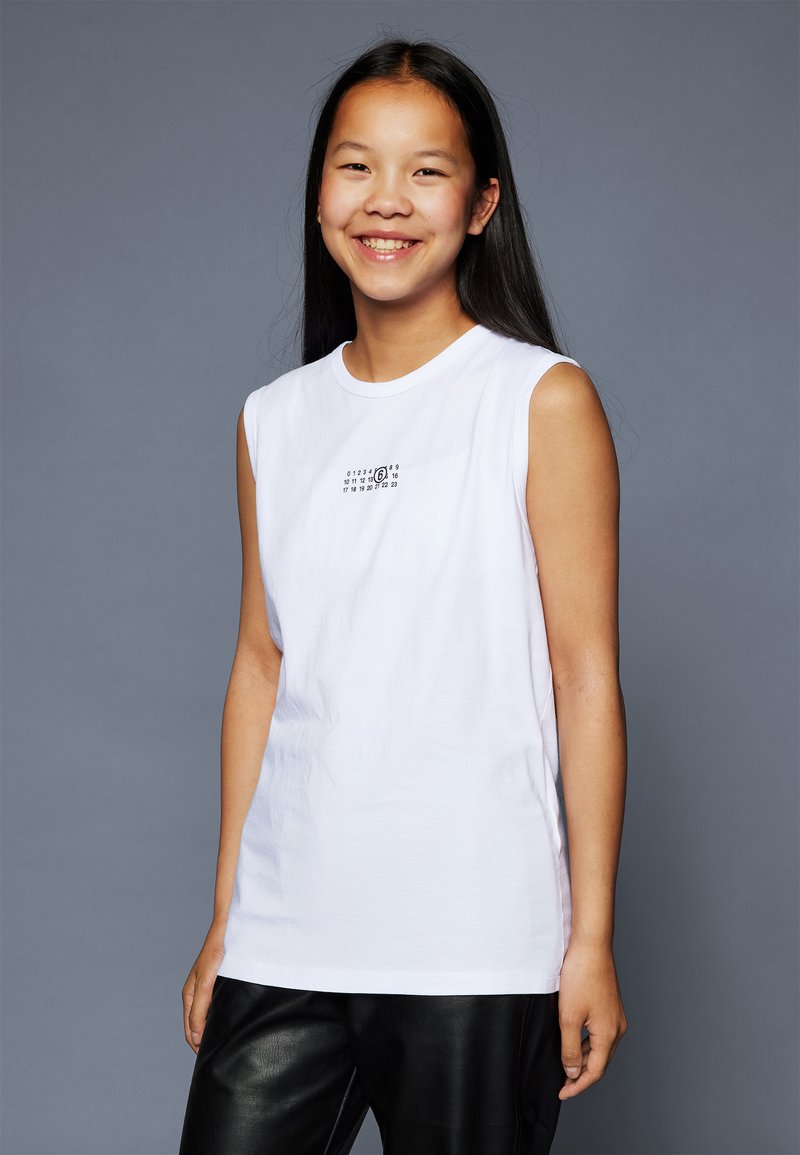 Vit ärmlös t-shirt i bomull, med en liten svart grafik framtill, rund halsringning och en avslappnad passform.