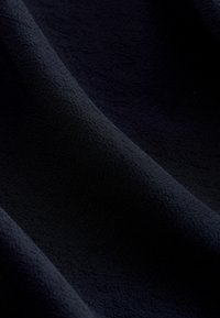 Tmavě modrá tkanina s hladkým, texturovaným povrchem, která obsahuje jemný vzor, jenž dodává hloubku a vizuální zajímavost. Měkký a flexibilní materiál.