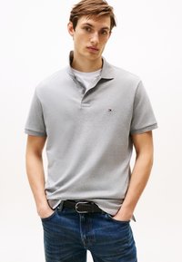 Polo gris à manches courtes avec col, orné d'un petit logo brodé. Associé à un jean bleu foncé et une ceinture noire texturée.