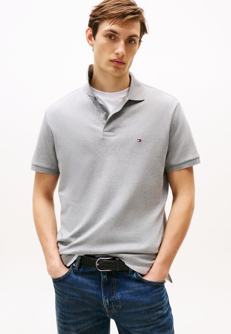 Polo gris à manches courtes avec col, orné d'un petit logo brodé. Associé à un jean bleu foncé et une ceinture noire texturée.