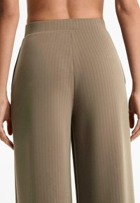 Beige, bordázott nadrág magas derékkal, oldalsó zsebekkel és laza szabással, hátulról bemutatva. Sima felület és igényes kialakítás.