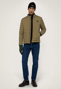 Khaki prošívaná bunda s vysokým límcem, černým zipem a bočními kapsami. Kombinováno s námořnickými džíny, černými rukavicemi a tmavými botami.