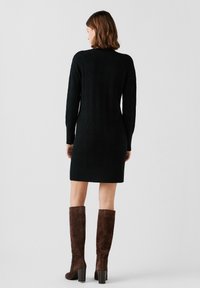 Zwarte gebreide jurk met een gestructureerd ruitpatroon, halverwege de dijlengte, gecombineerd met bruine suède laarzen tot de knie met een chunky hak.