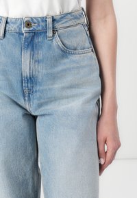Jeans de mezclilla de corte alto en azul claro con un ajuste relajado, que presentan bolsillos delanteros, un cierre de botón único y un ligero desgaste.