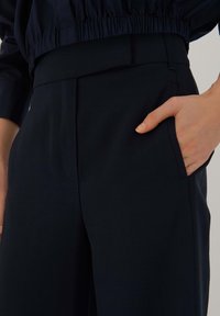 Mörkblå byxor med skräddarsydd design, slät yta, sidofickor och en platt midja, med elastiska detaljer upptill.