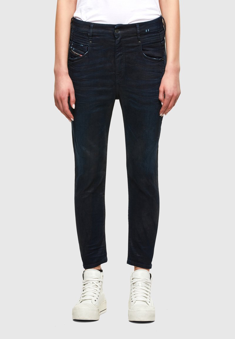 Jeans oscuros ajustados con un ligero desvanecimiento, que presentan bolsillos frontales y costuras decorativas. Combinados con zapatillas blancas de caña alta.
