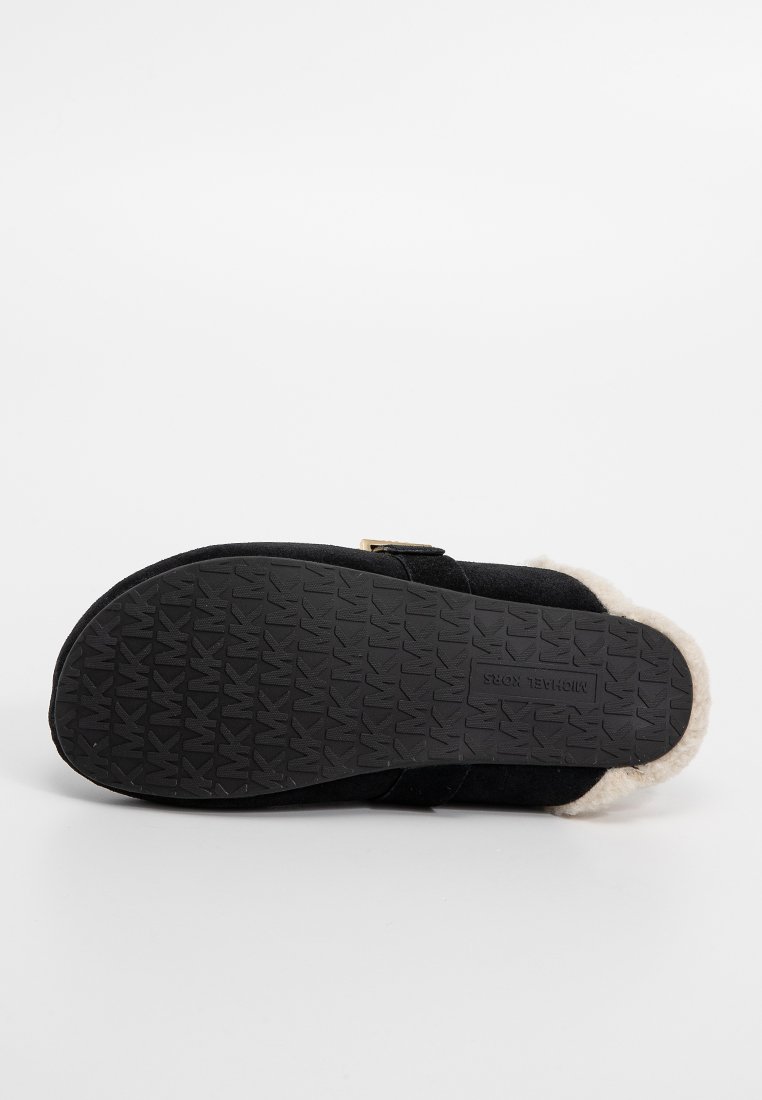 Pantoufle en suède noir avec une semelle en caoutchouc texturée, dotée d'un doux revêtement en crème et d'une simple sangle réglable.