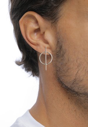 Boucle d'oreille en métal argenté dotée d'un design circulaire avec une barre verticale au centre. La finition est lisse et réfléchissante.