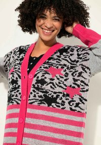 Cárdigan de punto con un diseño de estampado de leopardo en negro, blanco y rosa, con acentos a rayas, botones rosas y un cuello rosa en contraste.