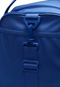 Blauwe sportduffel tas met een gestructureerd mesh-paneel, een grote ritssluiting en een plastic clipsluiting voor veilige bevestiging.