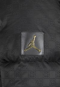 Sort pufferjakke med et tekstureret mønster af "23" og et metalguld Jumpman-logo på en sort læderlap.