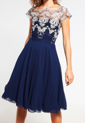 Robe bleu marine longueur genou avec manches courtes en dentelle transparente et broderie florale blanche complexe sur le corsage. Jupe évasée avec un doux tombé de tissu.