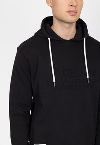 Felpa nera con cappuccio e logo in rilievo "DENIM PROJECT", lacci bianchi e finitura in tessuto testa di moro. Presenta una tasca a marsupio.