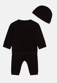 Crni, quiltani baby outfit s dugim rukavima i hlačama, s odgovarajućom kapicom. Mekani materijal s rebrastim manžetama i obrubima.