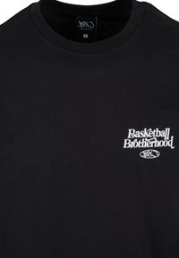 Czarna bawełniana koszulka z okrągłym dekoltem. Biała grafika z logo "Basketball Brotherhood" na lewej piersi. Minimalistyczny design, miękka faktura.