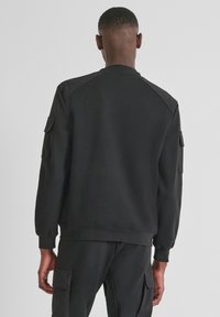 Felpa nera con scollo rotondo, maniche raglan e due tasche laterali; tessuto strutturato con finitura liscia; design minimalista.