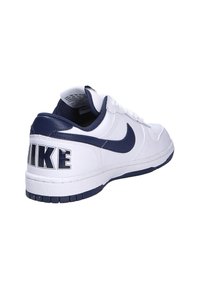 Baskets en cuir blanc avec des accents navy. Caractéristiques : bout rond, design à lacets, et "NIKE" imprimé en grandes lettres sur le talon.