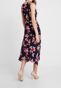 Robe florale avec une base bleu marine foncé, des motifs de fleurs roses et blanches, un design sans manches et un ourlet asymétrique. Assortie à des talons nus.