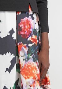 Svart åtsittande topp med kort ärm, ihopparad med en flerfärgad blomstertryckkjol med röda, rosa och gröna nyanser på en vit bakgrund.