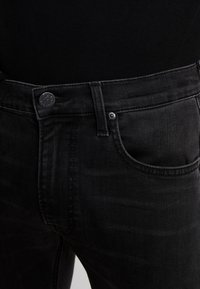 Vaqueros de denim negros con un corte ajustado, que presentan un cierre de botón y cremallera, detalles de costura sutiles y un diseño clásico de cinco bolsillos.