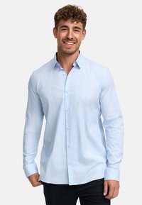 Camisa de botones de manga larga en azul claro, con un cuello extendido, puños de un solo botón y una tela suave, ligeramente texturizada.