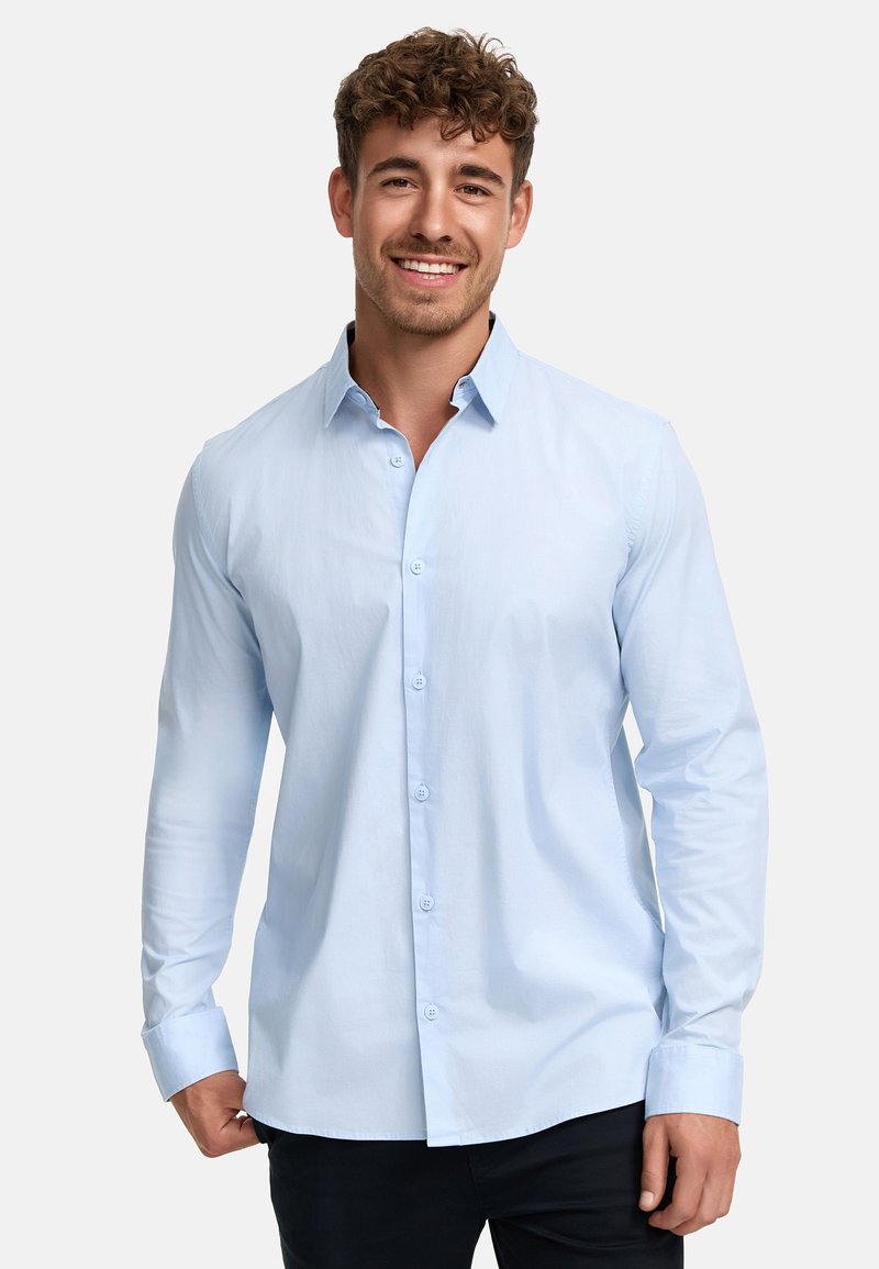 Chemise bleu clair à manches longues avec un col évasé, des poignets à un bouton et un tissu lisse, légèrement texturé.