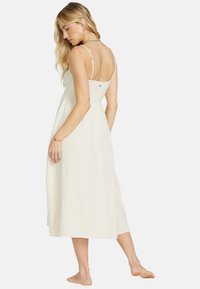 Kermavaalean midi-mekko, jossa ohuet olkaimet, teksturoitu kangas, istuva bodice ja valuva hame, jossa on hienovarainen takasuunnittelun yksityiskohta.