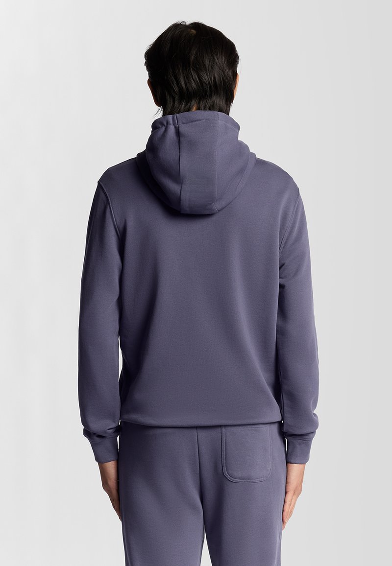 Felpa viola con una vestibilità comoda, cappuccio con coulisse e polsini a coste. Tessuto morbido, presenta una tasca sul retro dei pantaloni abbinati.