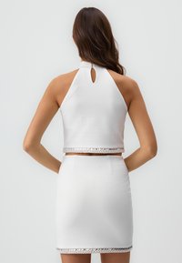 Ensemble comprenant un top halter blanc et une mini jupe, mettant en avant un dos à trou de serrure et un ourlet orné d'accents en perles transparentes, avec une texture lisse.