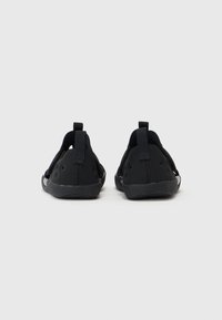 Černá obuv s texturovaným povrchem, síťovanými stranami a pevnou oporou paty. Obsahuje poutko na zadní straně pro snadné obouvání.