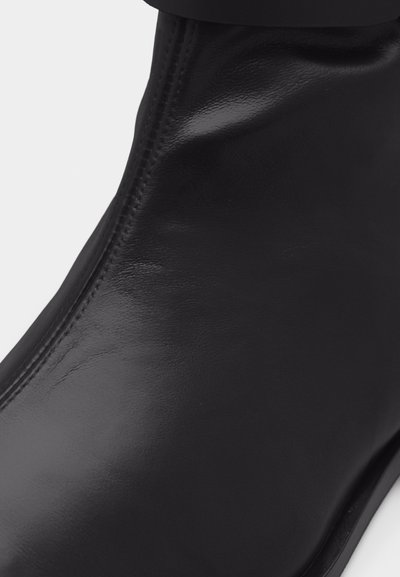 Κοντινή εικόνα ενός λείου μαύρου δερμάτινου μποτάκι με εμφανείς ραφές κατά μήκος της πλευράς και στρογγυλεμένο σχήμα μύτης.