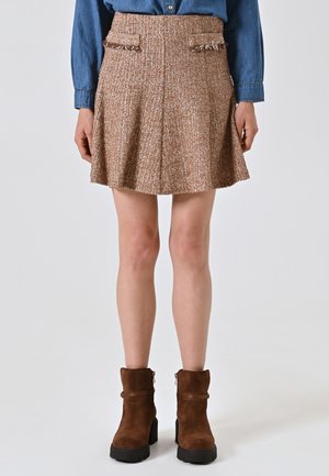 Gonna mini in tweed marrone con dettagli delle tasche sfilacciati e pieghe, abbinata a stivaletti alla caviglia in pelle scamosciata marrone con zip laterale e tacco grosso.
