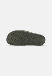 Tongs en caoutchouc avec une semelle intérieure texturée verte, dotées d'une semelle à motif en zigzag pour une meilleure adhérence et durabilité. Logo embossé sur la semelle.