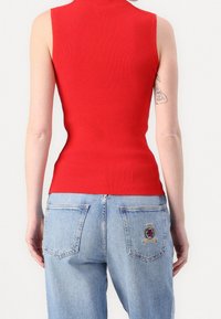 Röd ribbad ärmlös topp med hög krage, kombinerad med ljusblå denimjeans som har en broderad lapp på bakfickan.