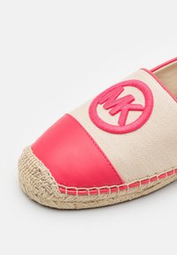Espadrille en toile avec un capuchon en cuir rose, mettant en avant un logo circulaire MK brodé et des détails en corde de jute le long de la semelle.