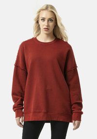 Rode longsleeve trui met een getextureerde afwerking, oversized pasvorm, ruwe randmouwen en een ronde halslijn. Gestyled met zwarte broek.