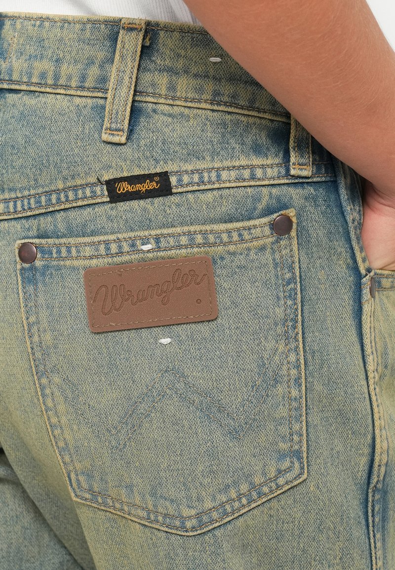Jeans in denim azzurro chiaro con un'etichetta in pelle del marchio Wrangler. Presentano cuciture doppie e un design classico delle tasche con rivetti.