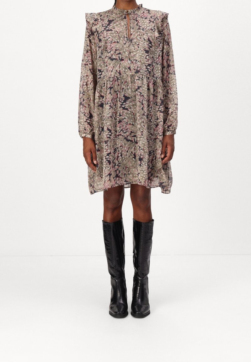 Femme portant une robe florale ample à manches longues avec un col goutte d'eau et des bottes en cuir noir texturé montantes jusqu'aux genoux.