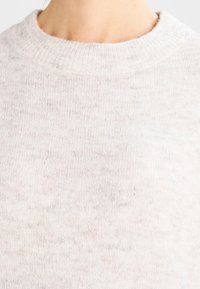 Lichtbeige gebreide trui met een ronde halslijn, zachte textuur en subtiele spikkelpatroon doorheen.