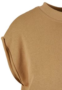 Gros plan d'une chemise beige à manches courtes avec un col rond côtelé et un détail de manchette cousu sur la manche.