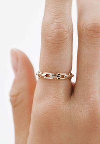 Anillo de cadena de plata con formas ovaladas y rectangulares interconectadas, con un acabado suave, llevado en un dedo sobre un fondo neutro.