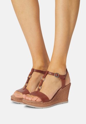 Sandales compensées marron avec une semelle texturée et tissée. Comprend une sangle au niveau des orteils et un design en T avec des accents en métal argenté et une sangle de cheville réglable.