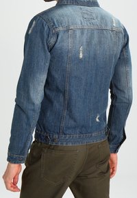 Jeansjacka i mörkblått med blekta områden och slitet detaljer; har klassisk krage, knäppning fram och två tryckknappar bak.