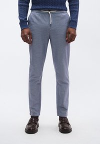 Ανοιχτό μπλε, στενά παντελόνια με ελαστική μέση με κορδόνι, φτιαγμένα από υφασμάτινο υλικό με υφή, συνδυασμένα με σκούρα καφέ παπούτσια χωρίς κορδόνια.