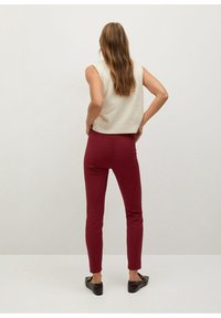 Krémový bezrukávový top s krátkým střihem, kombinovaný s úzkými bordovými kalhotami. Modelka má na sobě tmavé boty na slip a dlouhé vlasy.